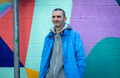 A man in a blue jacket standing in front of a colorful, geometric mural.
